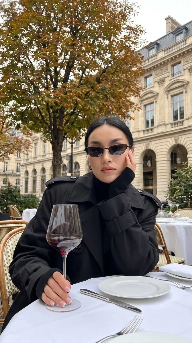 A woman in a black trench coat sitting at an outdoor cafe with wine. (2)