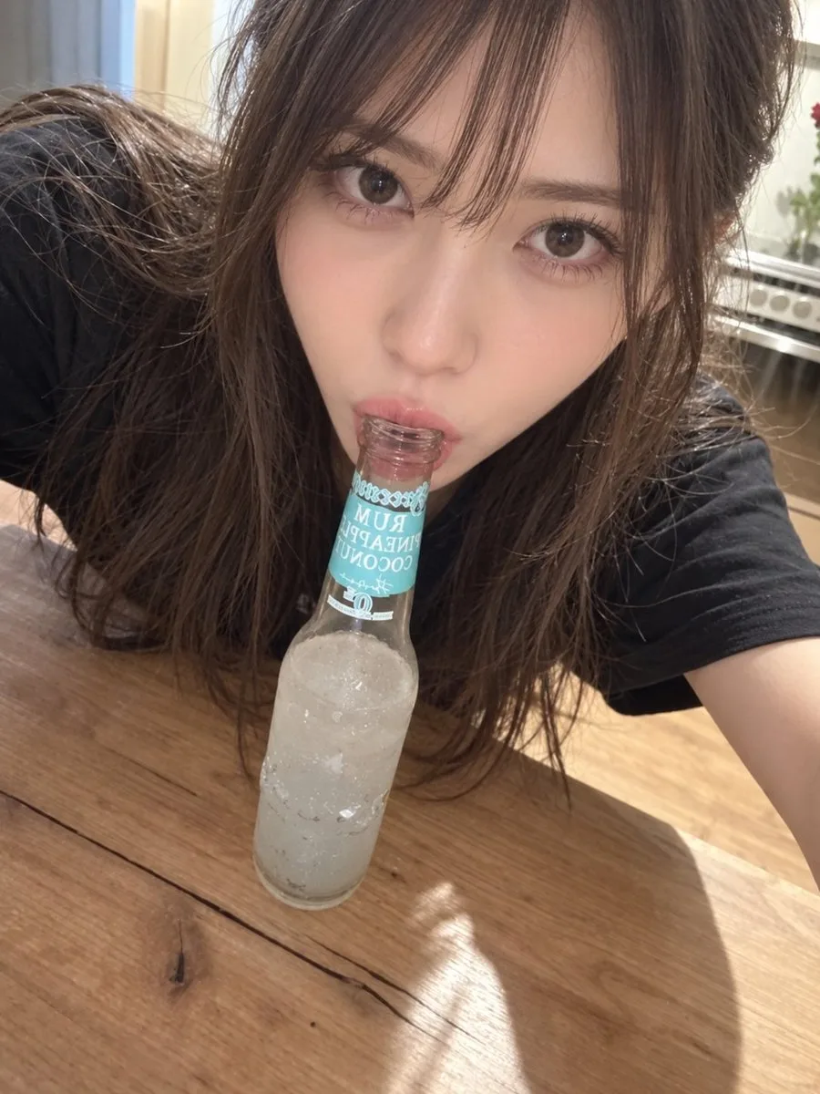 A young woman taking a selfie while touching her lips to a glass bottle.
