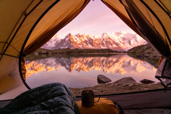 Cozy tent interior looking out at a stunning mountain sunrise and alpine lake.