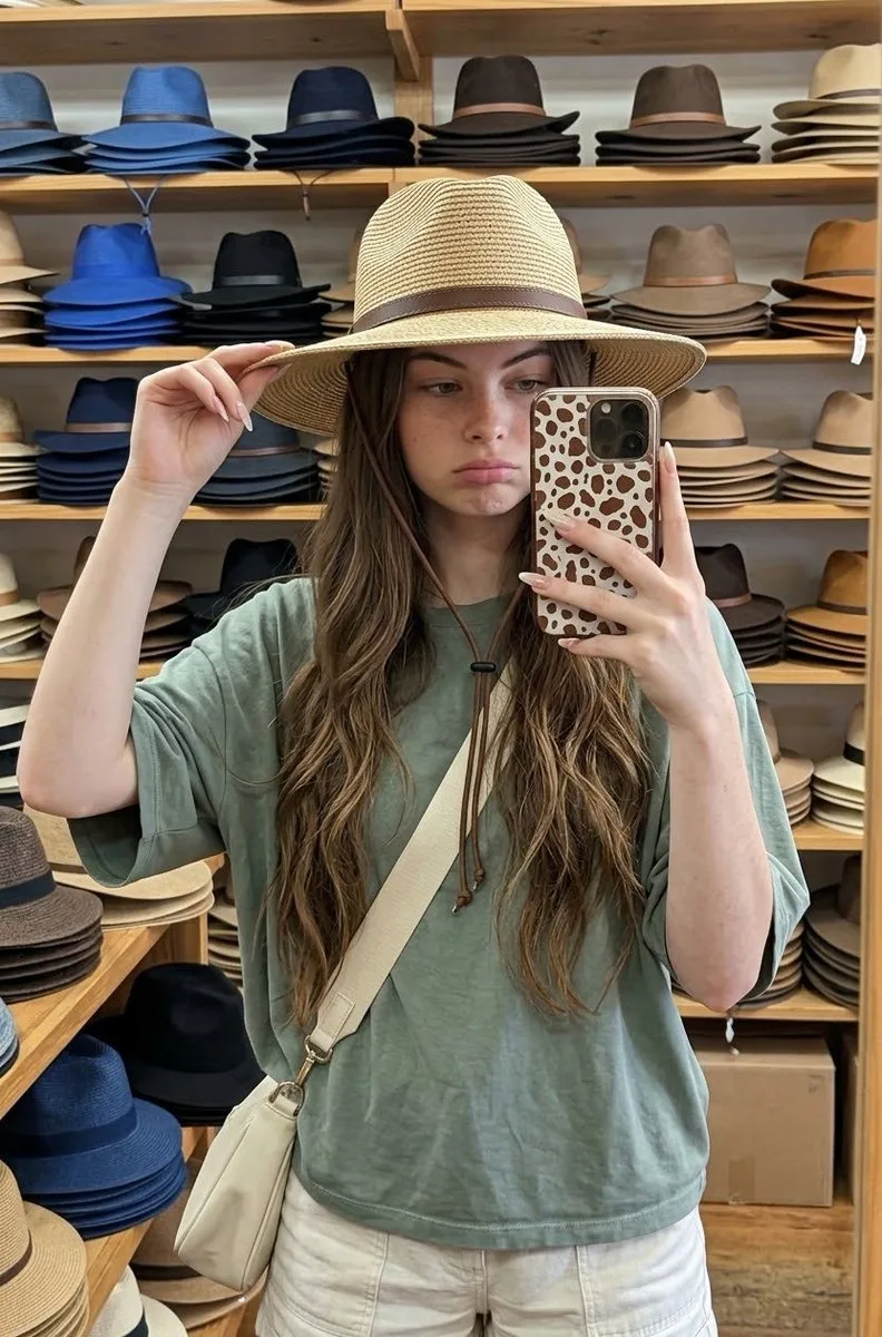 Woman taking a selfie while wearing a straw hat in a hat shop