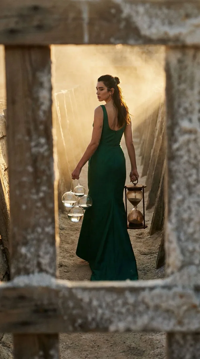 A person in a green gown walks away in a dusty salt trench carrying floating spheres.