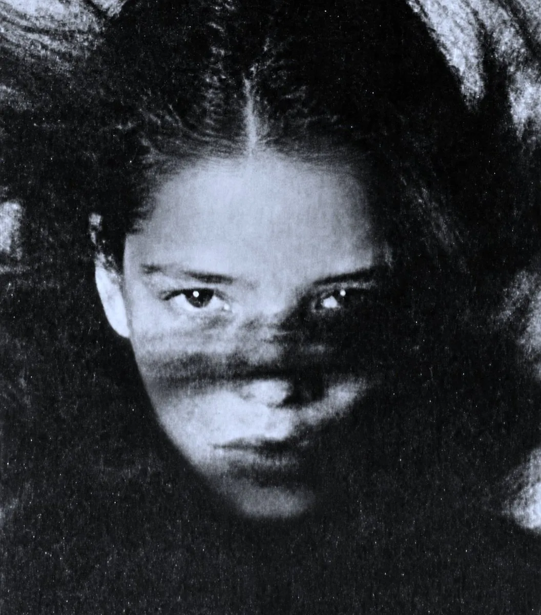 A grainy black and white portrait of a young woman with dark hair looking at the camera.