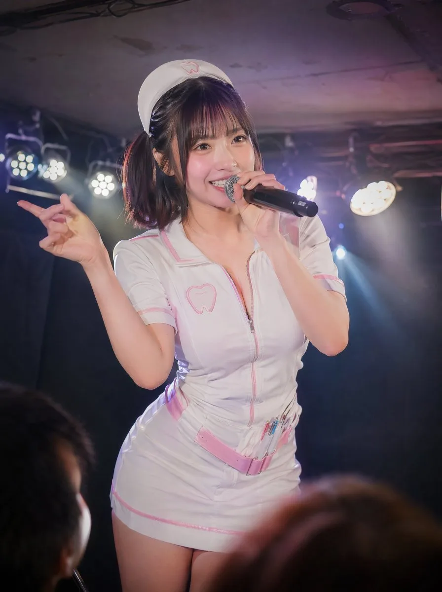 Japanese idol in a cute dental nurse costume performing on stage with a microphone