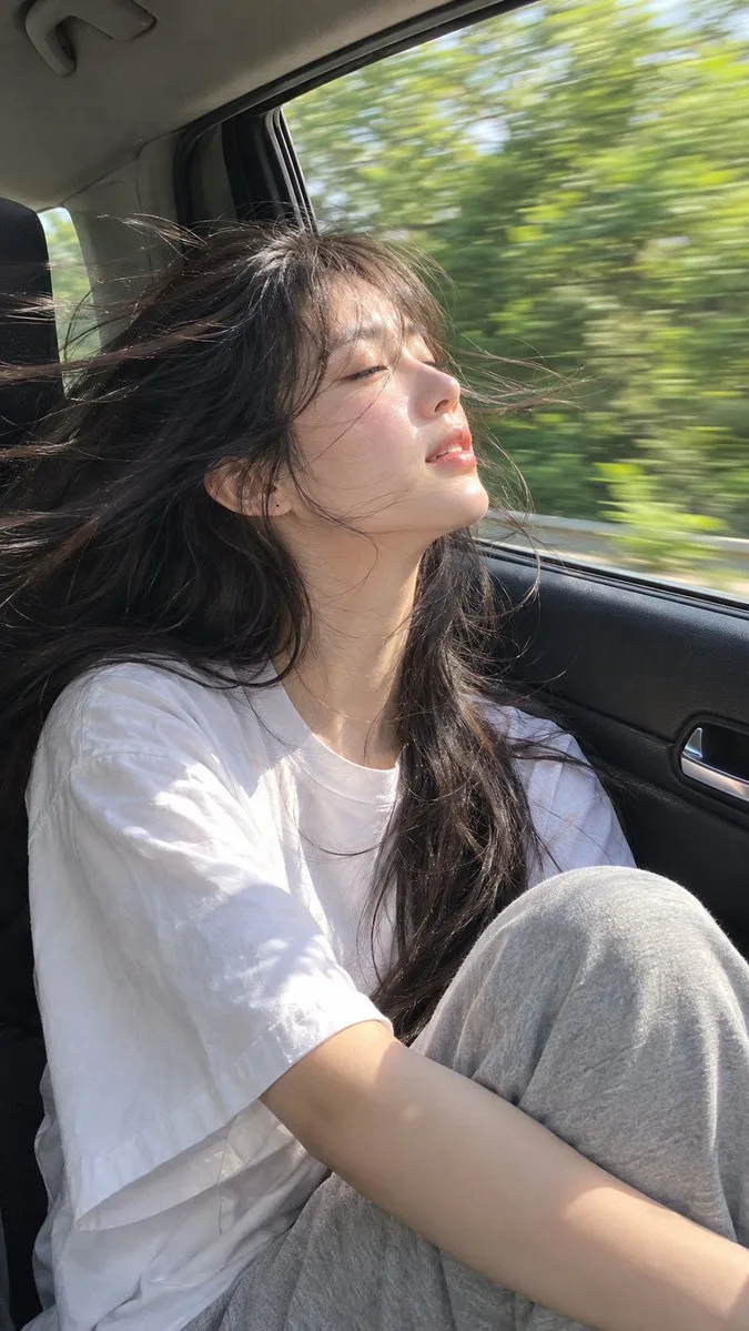 Woman in car, sunlight on face, hair blowing in wind.