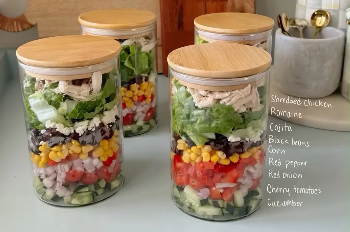 Four glass jars filled with layered Mexican chicken salad on a kitchen counter.