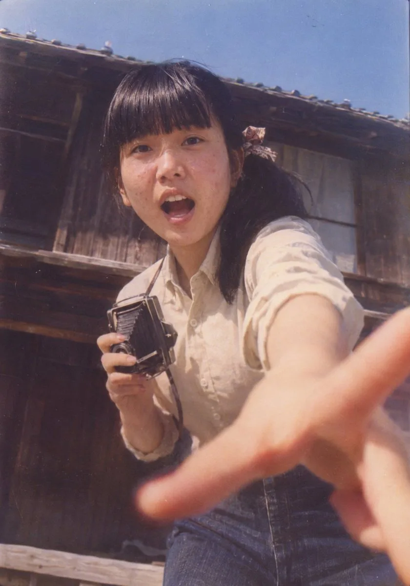 Retro photo of a surprised woman reaching toward the camera with a vintage bellows camera