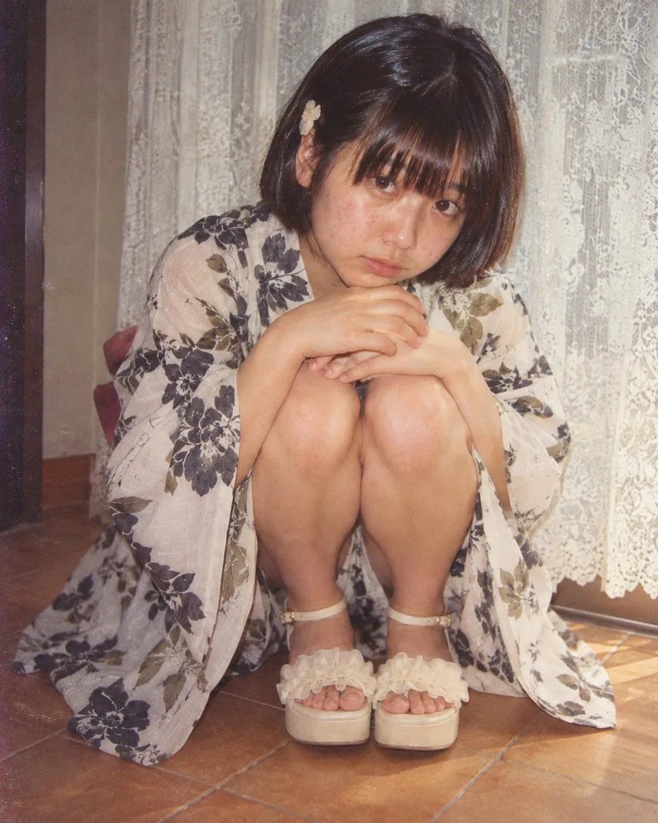 A melancholic woman in a floral kimono sitting on the floor with vintage film grain.