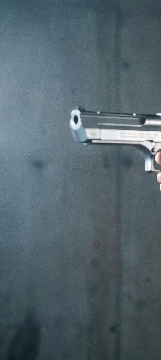 90s action heroine with platinum blonde hair aiming a pistol in an industrial setting.