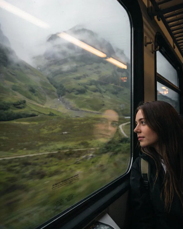 A young woman looking out a train window at misty mountains.