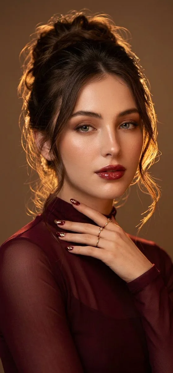 Elegant woman in a burgundy outfit with glowing skin and a sophisticated updo.