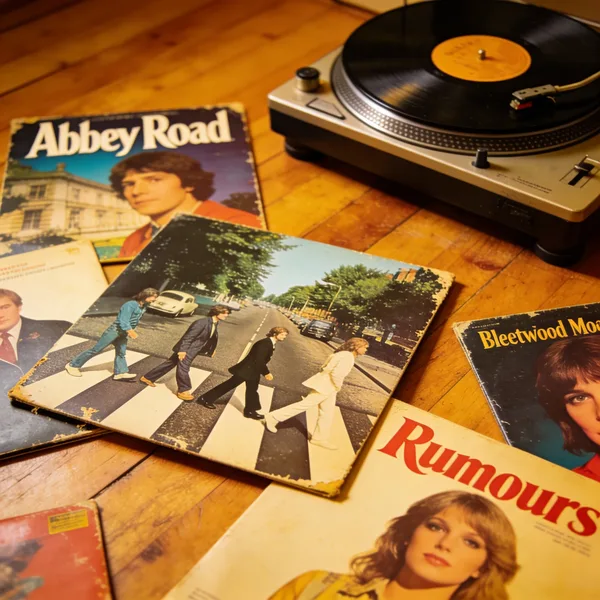 Vintage vinyl records and a record player on a wooden floor.
